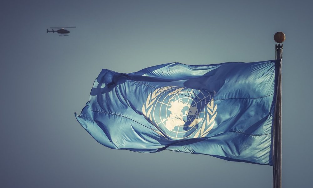 A UN blue flag captured flying in the wind at the United Nations Headquarters with a blurred helicopter on the background symbolizing a dedicated job of UN blue helmets serving in one of UN peacekeeping missions around the globe. Action for peacekeeping concept.
